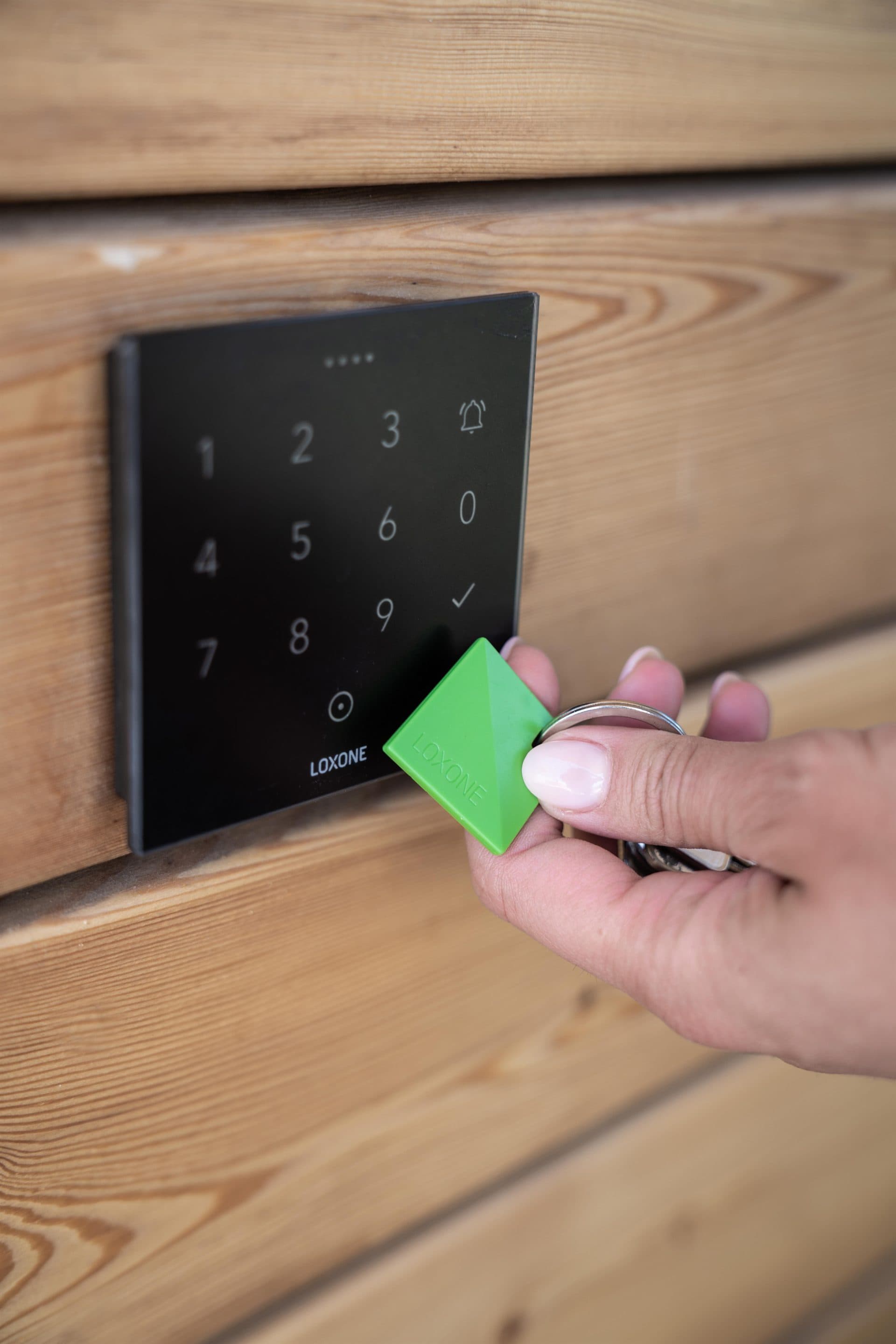 A hand presenting an NFC fob to an access keypad at a timber entrance
