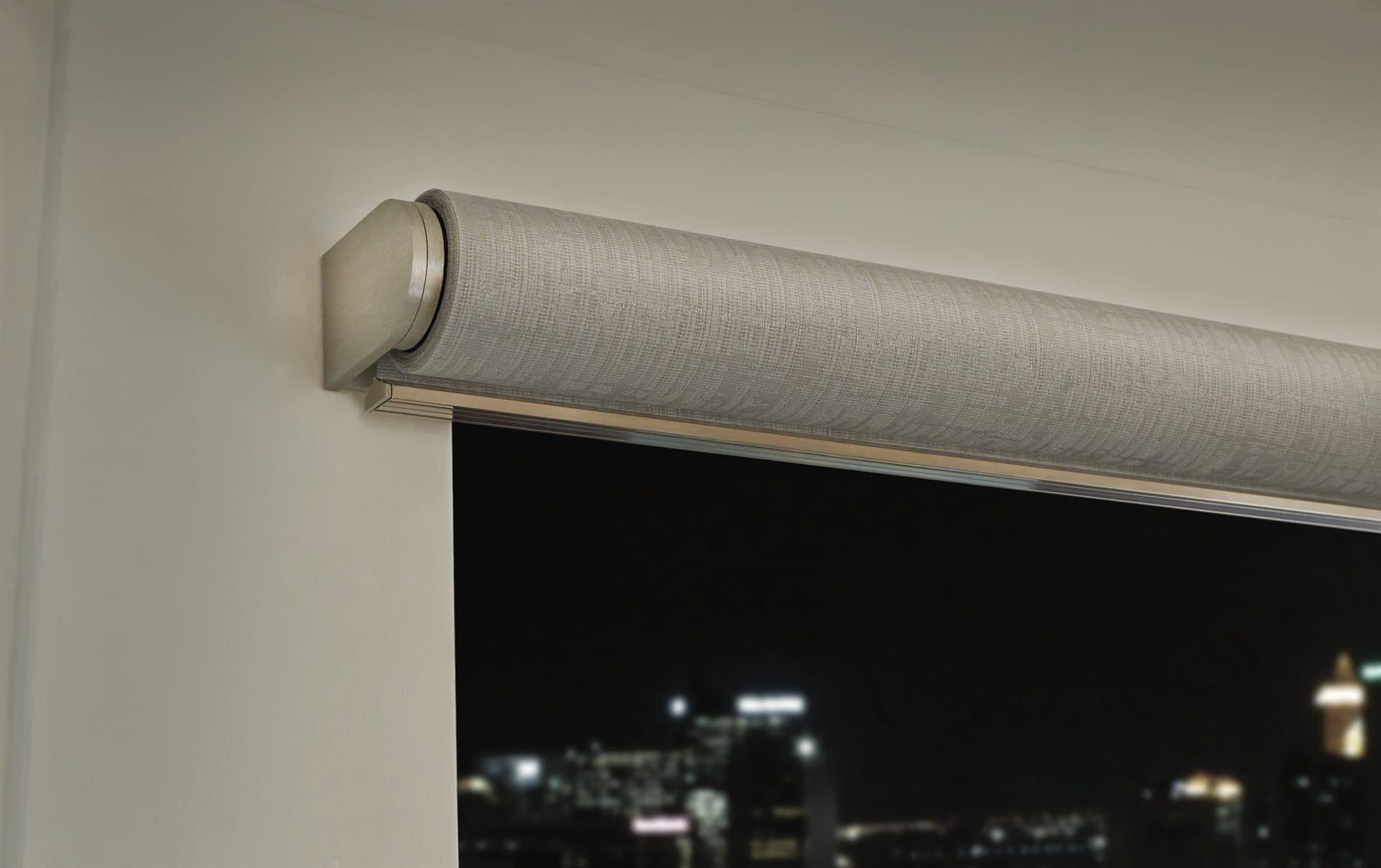 A discreet motorised roller blind lowered over a window with a night view