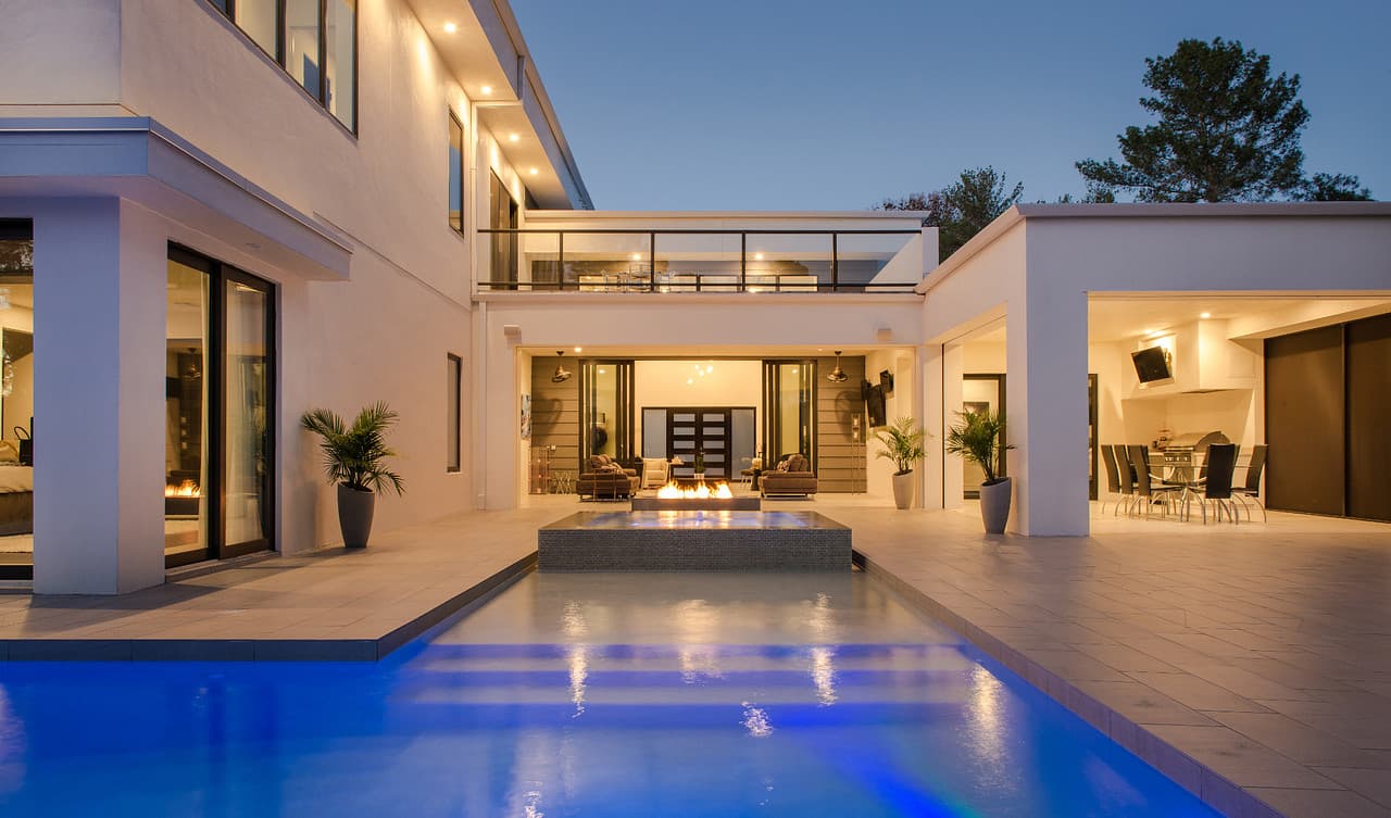 A luxury home at dusk with an illuminated infinity pool and fire features