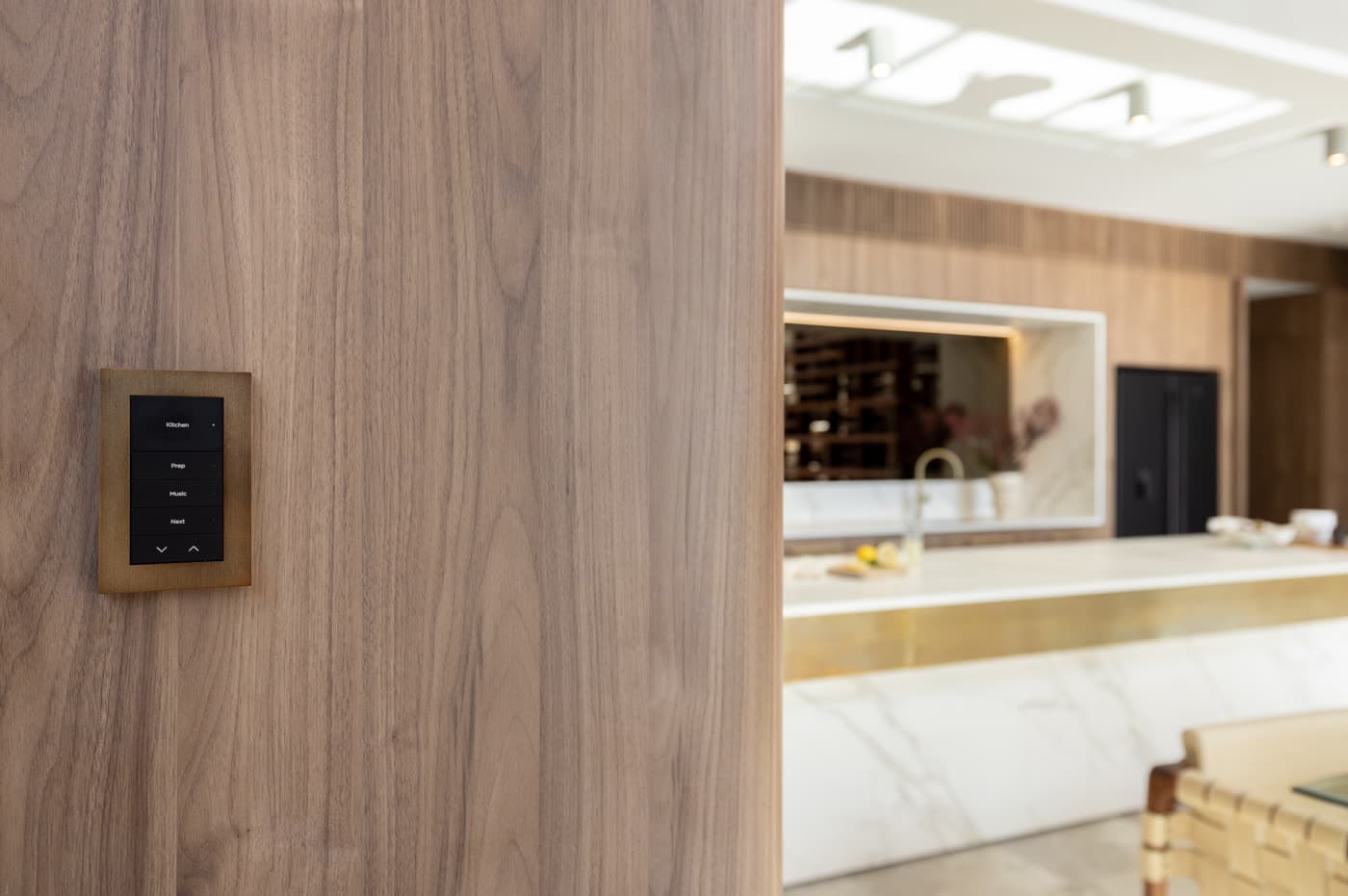 An engraved keypad set into a walnut wall beside an open-plan marble kitchen
