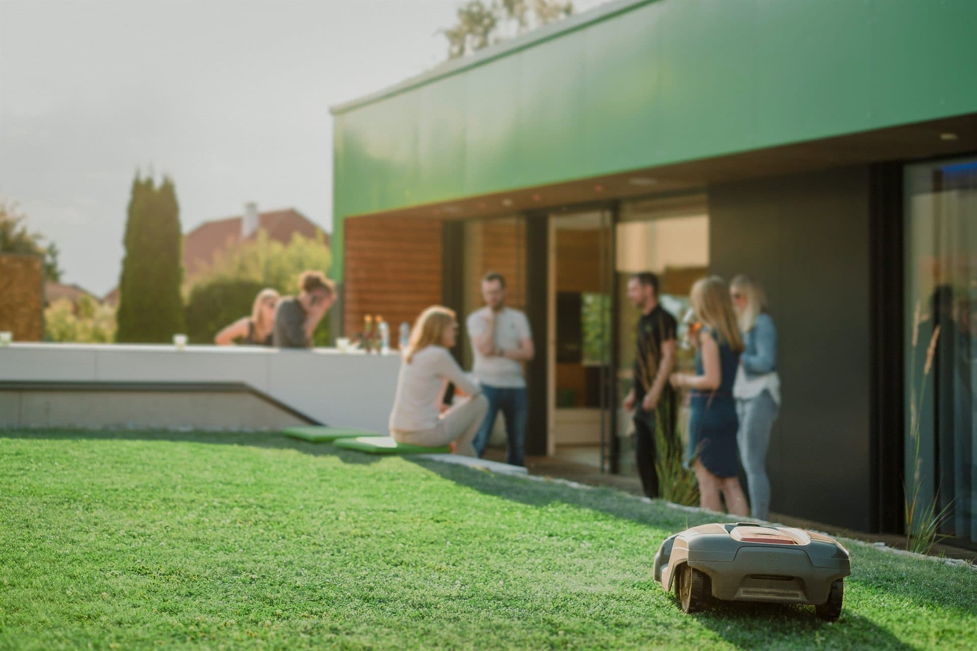 People relaxing on a terrace and lawn on a summer evening beside a lit garden